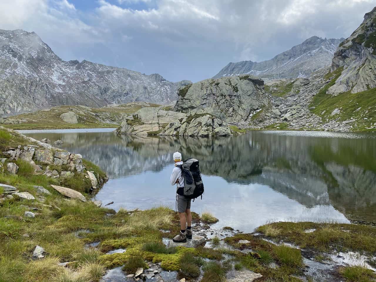 Bergsee in unberührter alpiner Landschaft, Mensch im Vordergrund geniesst die spezielle Stimmung